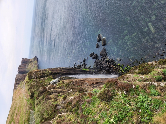Waterfall flowing into the ocean along a rocky coastline.