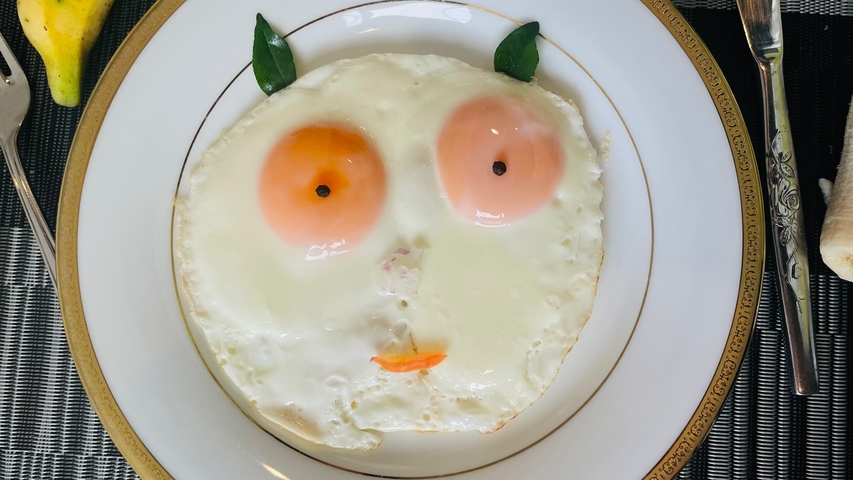 Plate with two sunny side up eggs arranged creatively with greens and tomatoes.