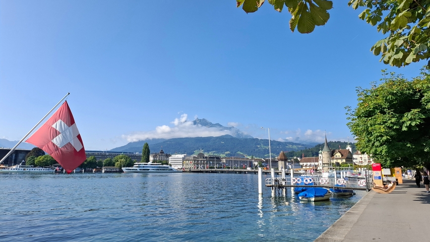 Swiss lake with mountains and buildings in the background and a Swiss flag.