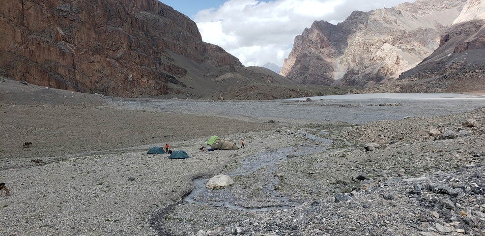       Campers set up tents in a rocky valley with distant mountains.
  