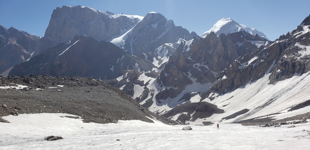       Hiker in a snowy mountain pass with peaks in the background.
  