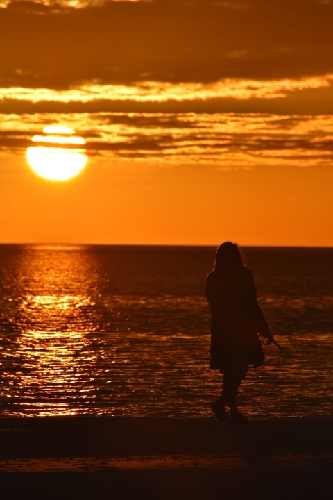       Silhouette of a person standing by the ocean during sunset.
  