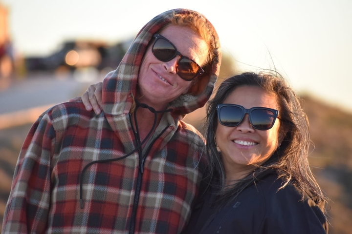       Two people smiling and hugging on a sunny day.
  