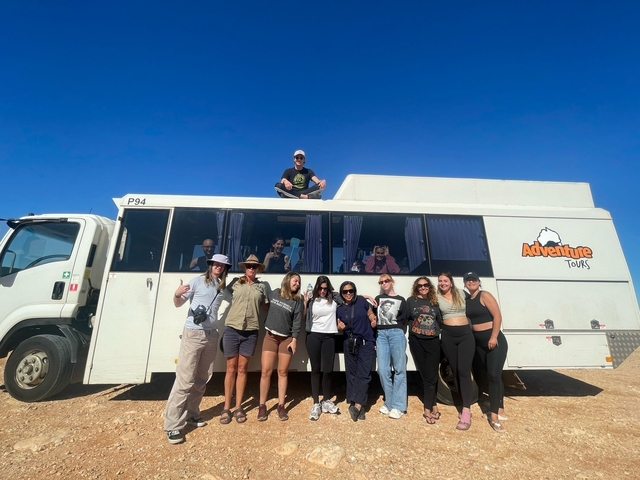       Group of people posing by a large touring vehicle.
  