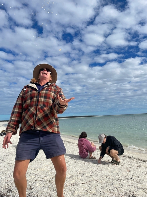       Person joyfully tossing an object by the beach.
  
