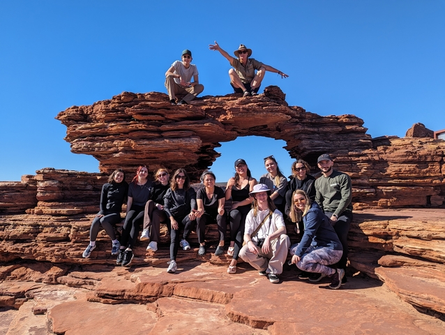       Group posing on red rock formation with a natural arch.
  