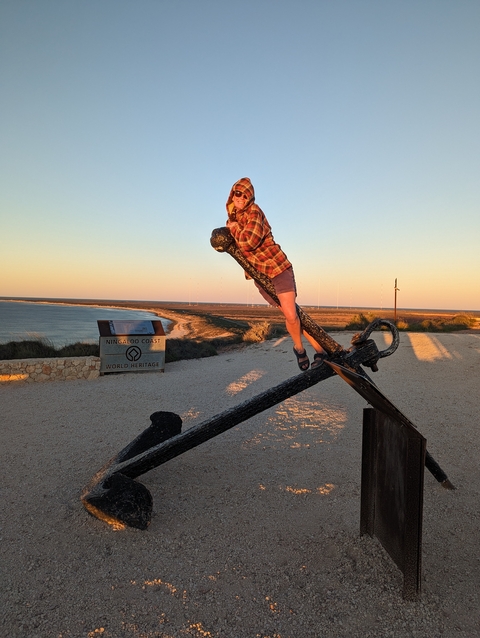      Person posing on a large metal anchor at sunset.
  