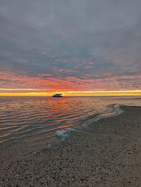       A beautiful sunset over the ocean with a boat in the distance.
  