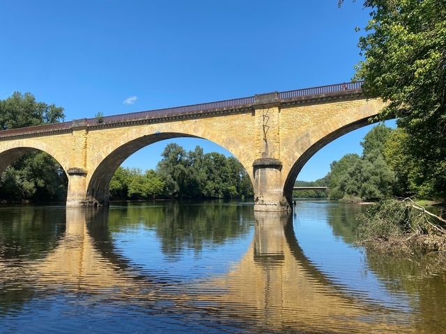 Stone bridge spanning over calm river waters amidst trees.