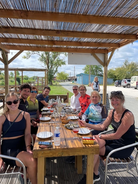 Group of people sitting at a table outdoors, enjoying a meal.