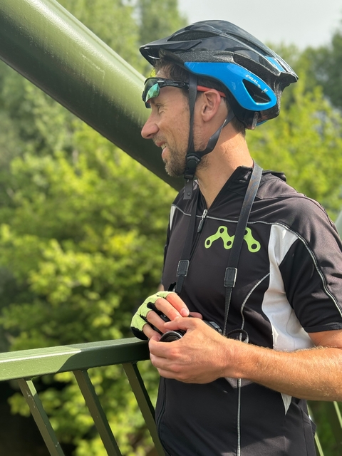 Man wearing a cycling helmet and gear, holding a water bottle.