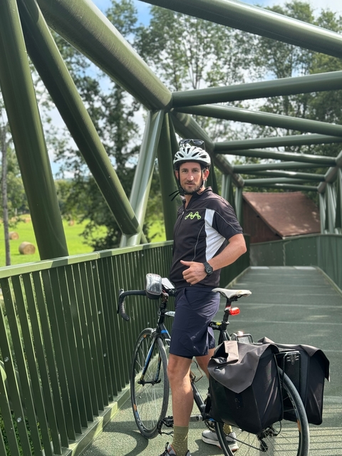 Man standing with a bicycle on a bridge.