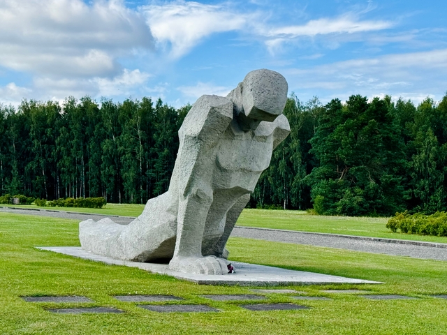       Large stone statue in a grassy park with forest background.
  
