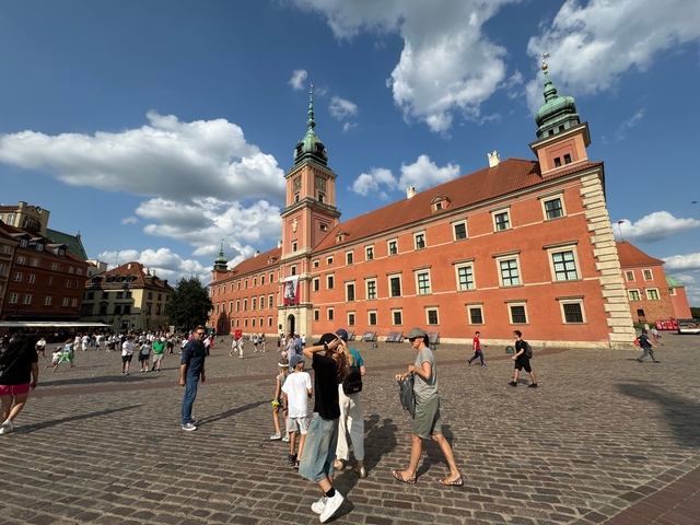       Colorful palace in Warsaw, Poland with people strolling in front.
  
