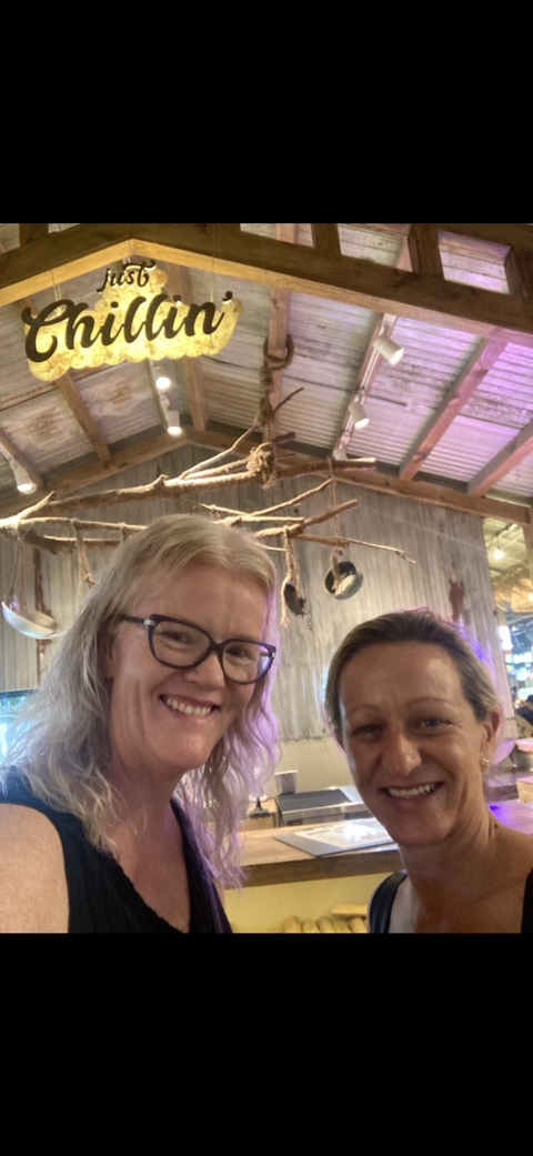 Two women smiling indoors with a rustic background.