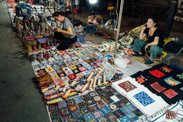 Market scene with women selling colorful fabrics and crafts.