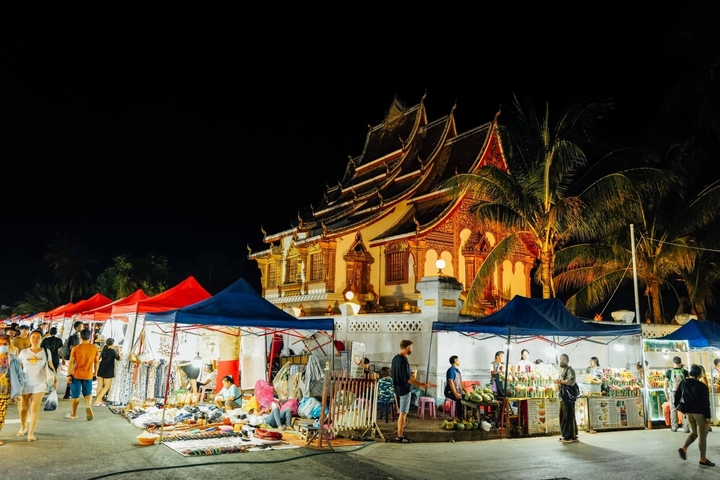 Night market with stalls and illuminated temple in the background.