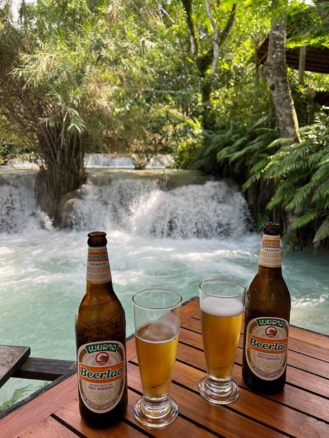 Beer bottles and glasses on a table with a waterfall in the background.