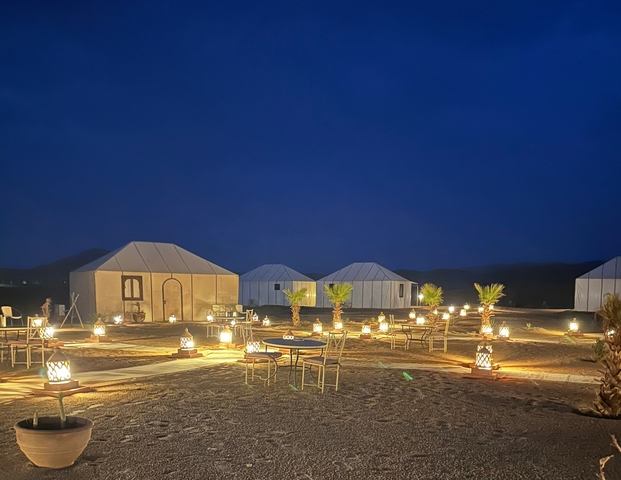       Outdoor dining setup with tents and lights at night in a desert setting.
  