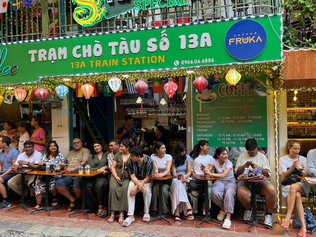 Group of people sitting on chairs outside a shop with signage in Vietnamese.