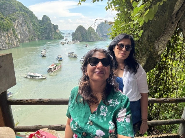       Two women posing in front of a scenic bay filled with boats and limestone karsts.
  