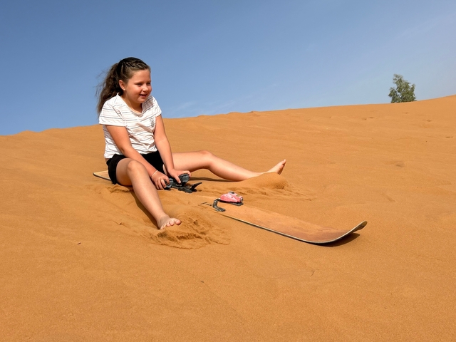       Child sandboarding on a desert dune.
  