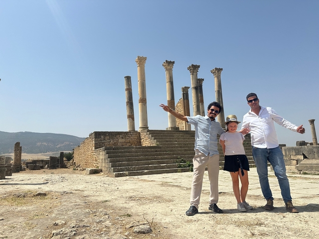       People posing in front of ancient ruins with columns.
  