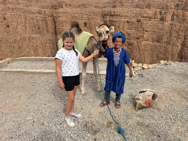       Children posing with a camel on a rocky terrain.
  