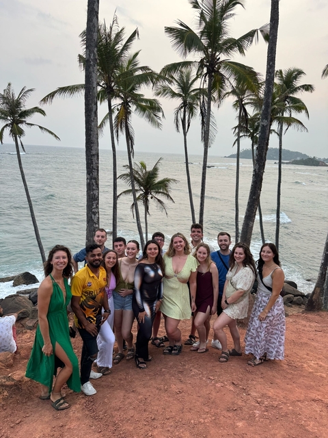       Group of people posing in front of palm trees with the ocean in the background.
  