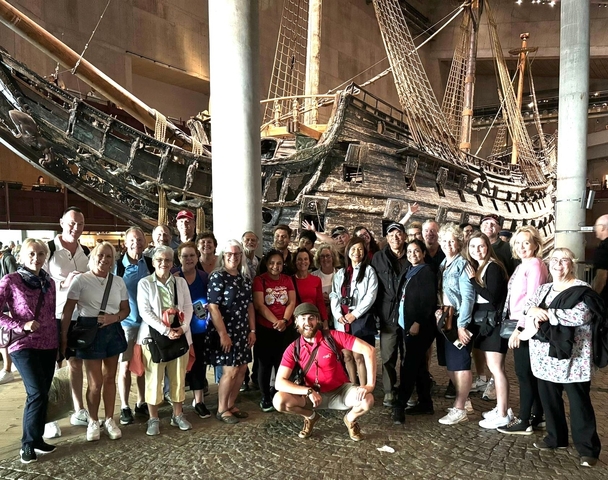 Group of tourists posing in front of a historic ship inside a museum.