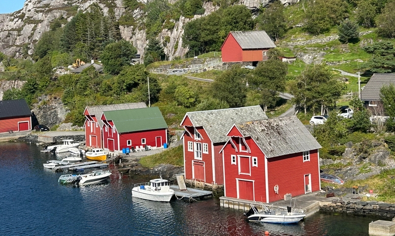 Red wooden boathouses by the water in a picturesque setting.