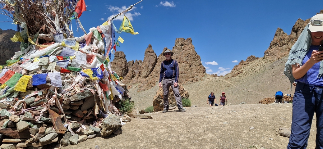 People walking past a cairn with flags in a rocky landscape.