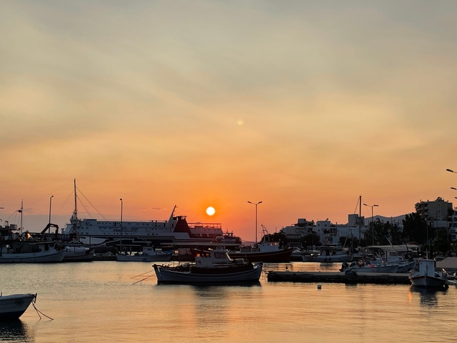       Sunset over a harbor with boats and buildings.
  