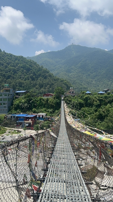 Suspension bridge with flags and buildings in the background in Nepal.