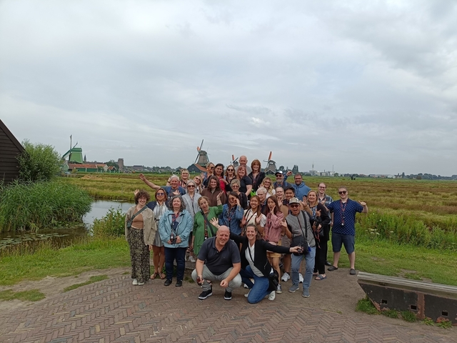Group of tourists posing with windmills in the background.