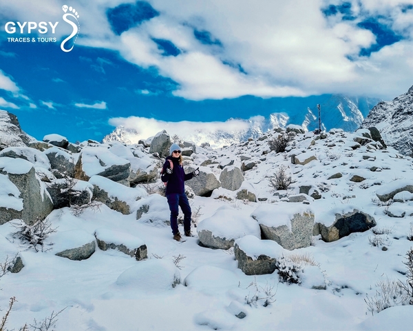      Person standing in snow-covered rocky terrain with mountains in the background.
  