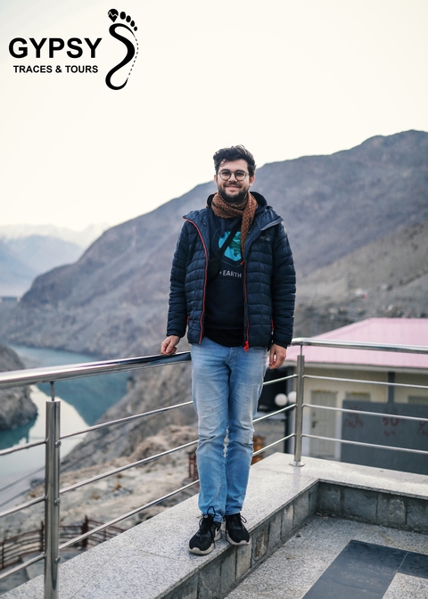       A person standing by a railing with mountains in the background.
  