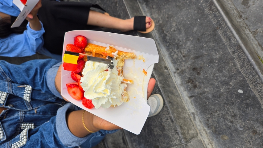 A hand holding a waffle with strawberries and cream.