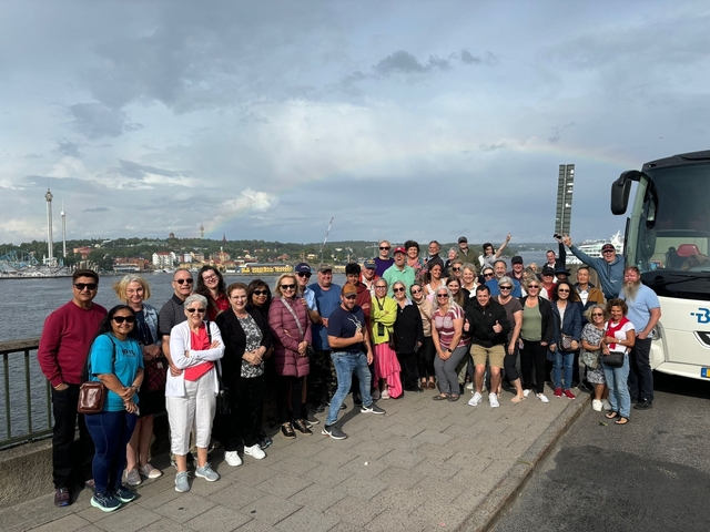       Group of people posing by a harbor with a bus visible.
  