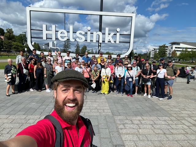       Group of people posing under a Helsinki sign.
  