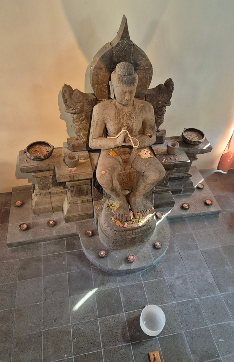 Statue with offerings placed around it in an interior setting.
