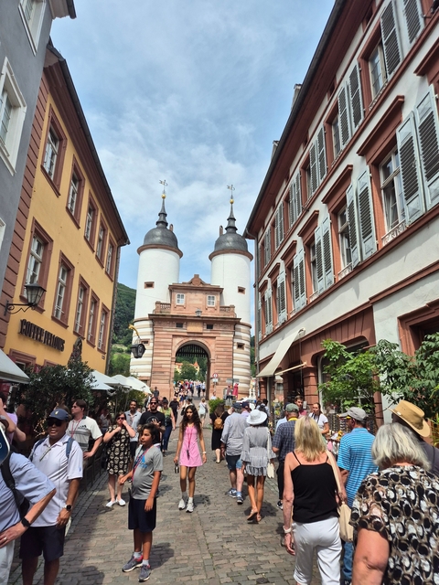 Historic gate with spires surrounded by people and shops.