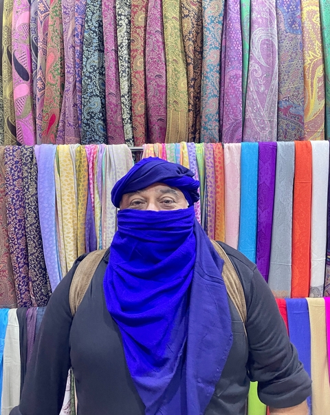       Man in traditional clothing in front of colorful fabrics.
  