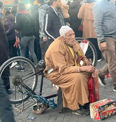       Older man with a hat sitting on a cart.
  