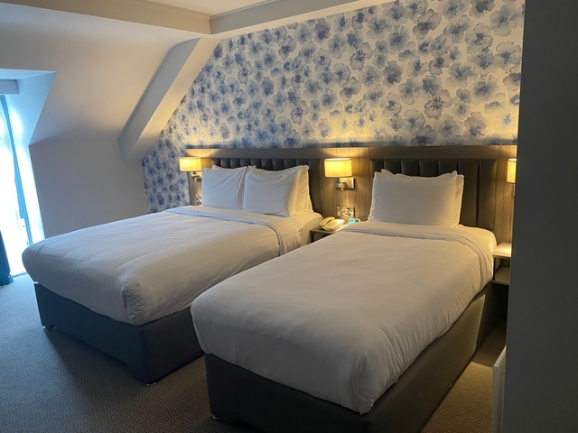 Two double beds in a hotel room with patterned wallpaper.
