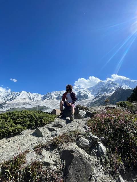 Person sitting on a rock with snow-capped mountains in the background.