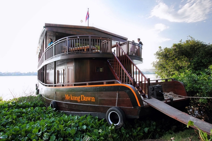 Wooden riverboat named 'Mekong Dawn' near vegetation