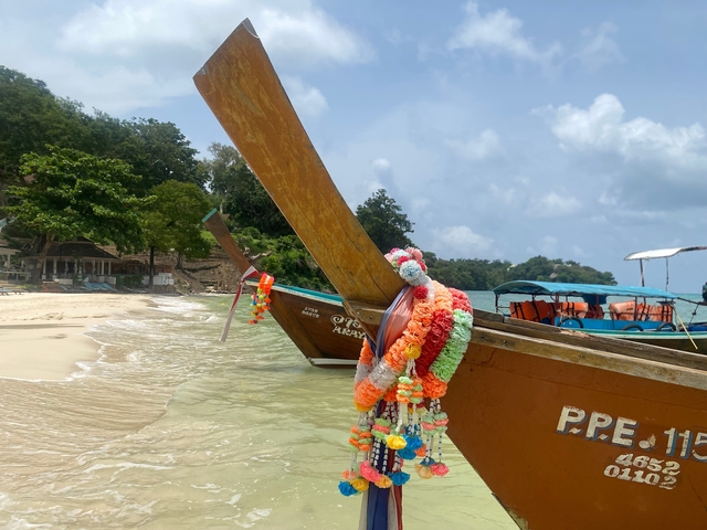       Longtail boats on the beach with decorations.
  