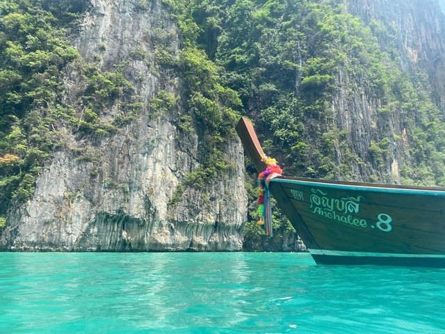 Longtail boat beside cliffs on clear turquoise water.