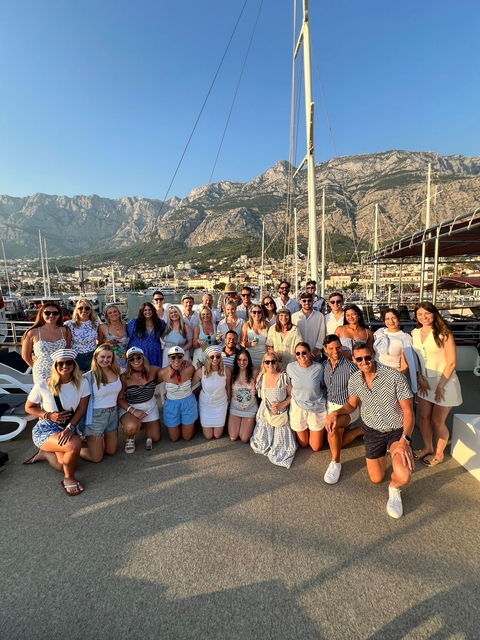       Group of tourists in front of a harbor with mountains.
  